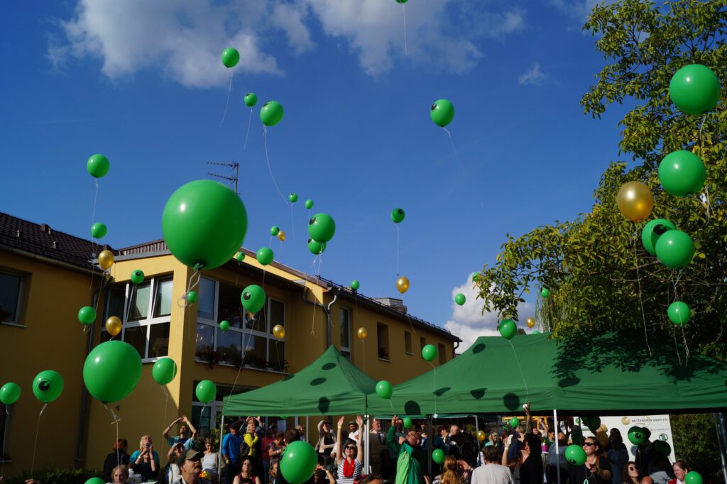 Menschen lassen grüne Luftballons vor dem Stadtteilzentrum Kaulsdorf steigen