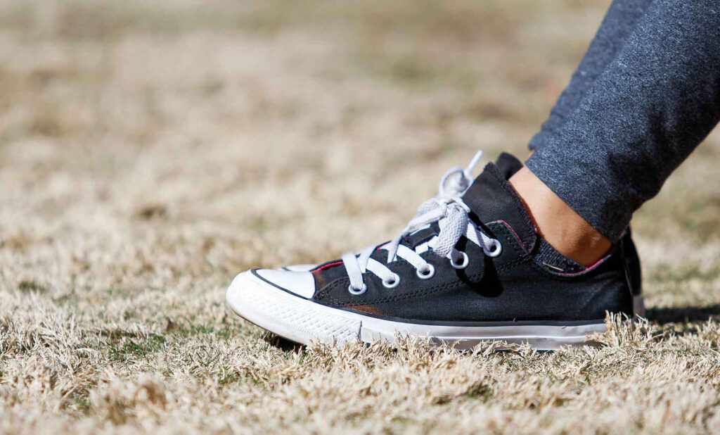 Fuß mit Schwarzem Schuh (Chuck) mit weißen Schnürsenkel im verbrannten Gras