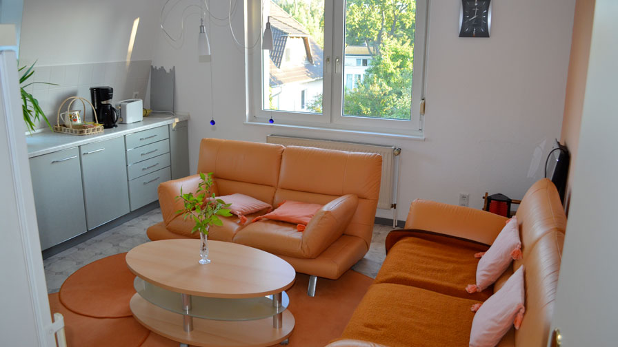 Gemeinschaftraum TWG Rüsternallee - Orangefarbene Couch, weiße Schrankzeile, runder Holztisch