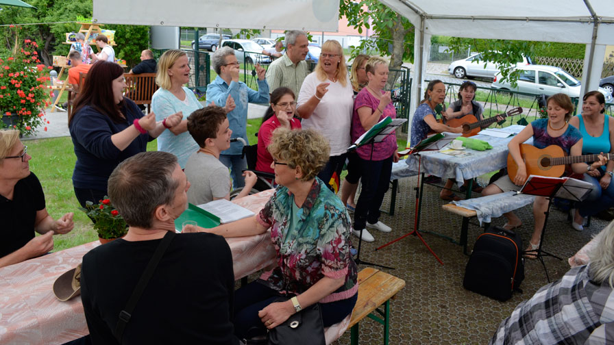 Singegruppe: In einem kleinen Festzelt singt die Singegruppe. Gäste sitzen auf Bierbänken und hören zu