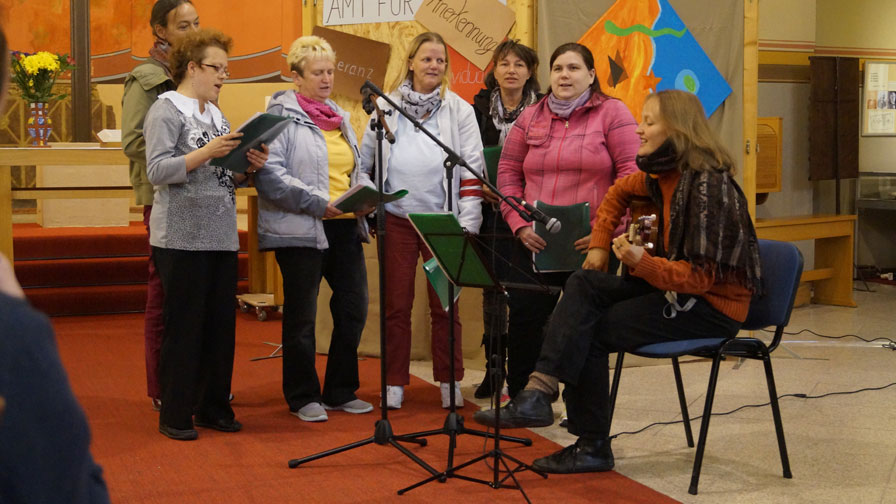 Singegruppe: 5 Sängerrinnen stehend und eine Gitarrenspielerin sitzend auf einer kleinen Veranstaltungsfläche