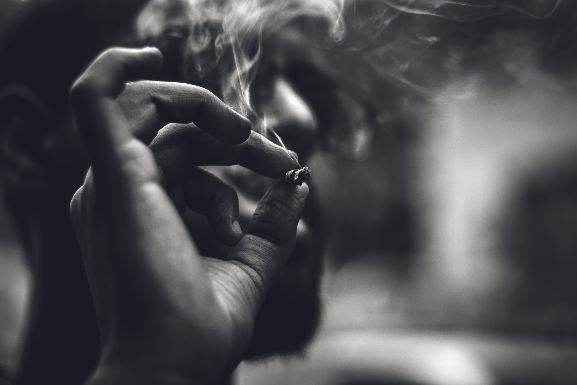 Sucht: Eine Hand hält eine Zigarette. Es qualmt. Bild ist schwarz-weiß